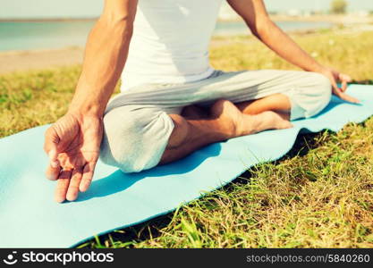 fitness, sport, people and lifestyle concept - close up of man making yoga exercises on mat outdoors