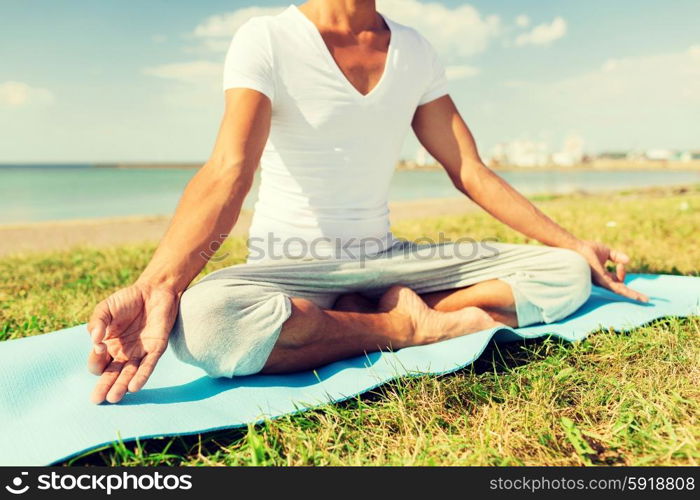 fitness, sport, people and lifestyle concept - close up of man making yoga exercises on mat outdoors