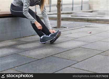 fitness, sport, people and lifestyle concept - close up of young sporty woman tying shoes outdoors
