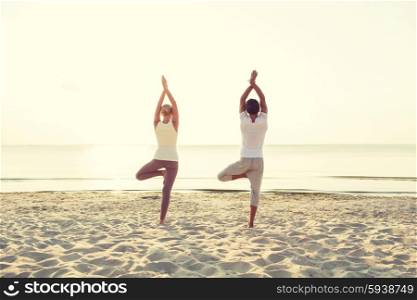 fitness, sport, people and lifestyle concept - couple making yoga exercises on sand outdoors from back