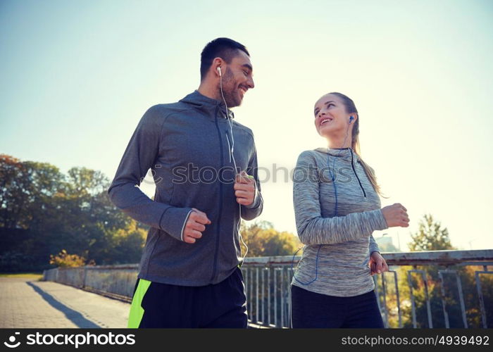 fitness, sport, people and lifestyle concept - happy couple with earphones running outdoors. happy couple with earphones running outdoors