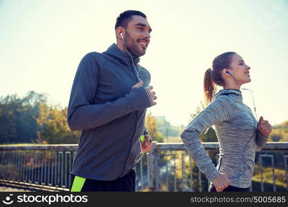 fitness, sport, people and lifestyle concept - happy couple with earphones running outdoors. happy couple with earphones running outdoors