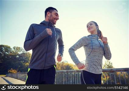 fitness, sport, people and lifestyle concept - happy couple with earphones running outdoors. happy couple with earphones running outdoors