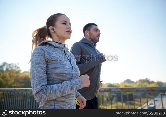 fitness, sport, people and lifestyle concept - happy couple with earphones running outdoors