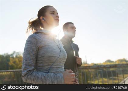 fitness, sport, people and lifestyle concept - happy couple with earphones running outdoors