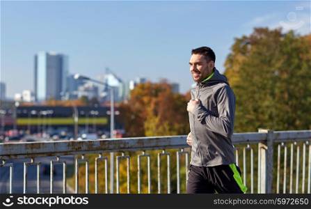 fitness, sport, people and lifestyle concept - happy young man running over city bridge