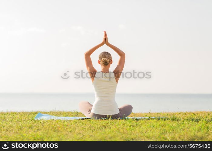 fitness, sport, people and lifestyle concept - of woman making yoga exercises on mat outdoors from back