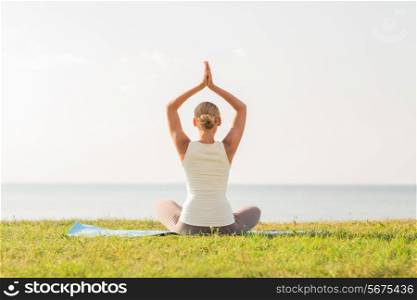 fitness, sport, people and lifestyle concept - of woman making yoga exercises on mat outdoors from back