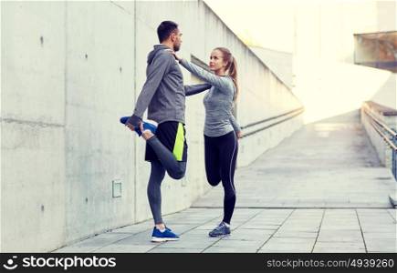 fitness, sport, people and lifestyle concept - smiling couple stretching leg outdoors. smiling couple stretching leg outdoors