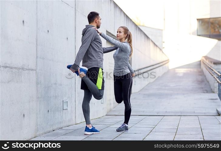 fitness, sport, people and lifestyle concept - smiling couple stretching leg outdoors