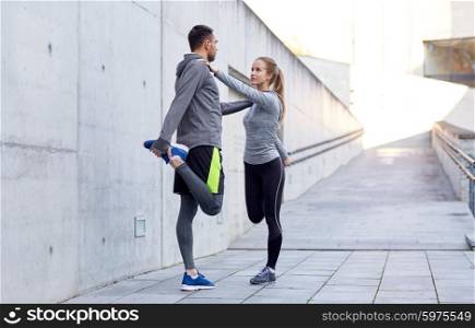 fitness, sport, people and lifestyle concept - smiling couple stretching leg outdoors