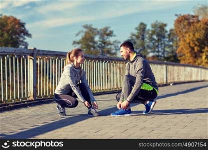 fitness, sport, people and lifestyle concept - smiling couple tying shoelaces outdoors. smiling couple tying shoelaces outdoors