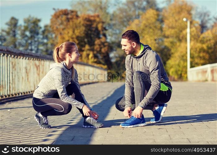 fitness, sport, people and lifestyle concept - smiling couple tying shoelaces outdoors. smiling couple tying shoelaces outdoors
