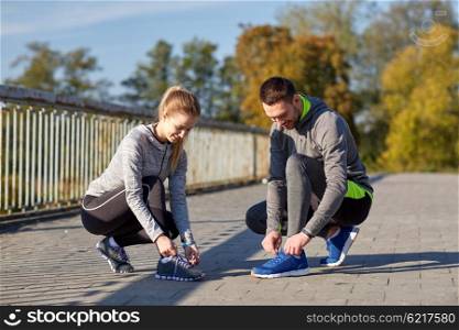 fitness, sport, people and lifestyle concept - smiling couple tying shoelaces outdoors