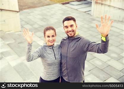 fitness, sport, people and lifestyle concept - smiling couple waving hands outdoors on city street. happy couple waving hands outdoors on city street