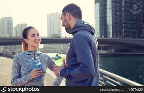 fitness, sport, people and lifestyle concept - smiling couple with bottles of water outdoors over dubai city street background. smiling couple with bottles of water in city