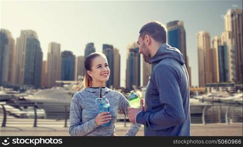 fitness, sport, people and lifestyle concept - smiling couple with bottles of water outdoors over dubai city street background. smiling couple with bottles of water in city