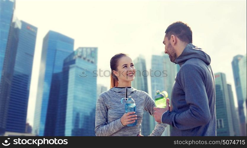 fitness, sport, people and lifestyle concept - smiling couple with bottles of water training over singapore city skyscrapers background. smiling couple with bottles of water outdoors