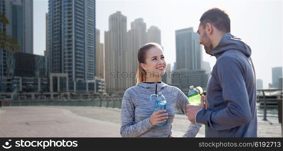 fitness, sport, people and lifestyle concept - smiling couple with bottles of water outdoors over dubai city street background