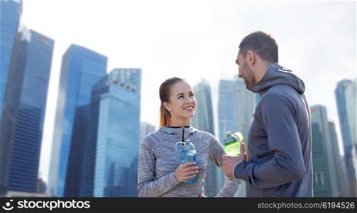 fitness, sport, people and lifestyle concept - smiling couple with bottles of water training over singapore city skyscrapers background