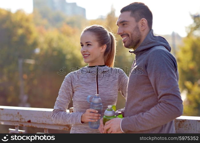 fitness, sport, people and lifestyle concept - smiling couple with bottles of water outdoors