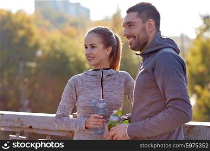fitness, sport, people and lifestyle concept - smiling couple with bottles of water outdoors
