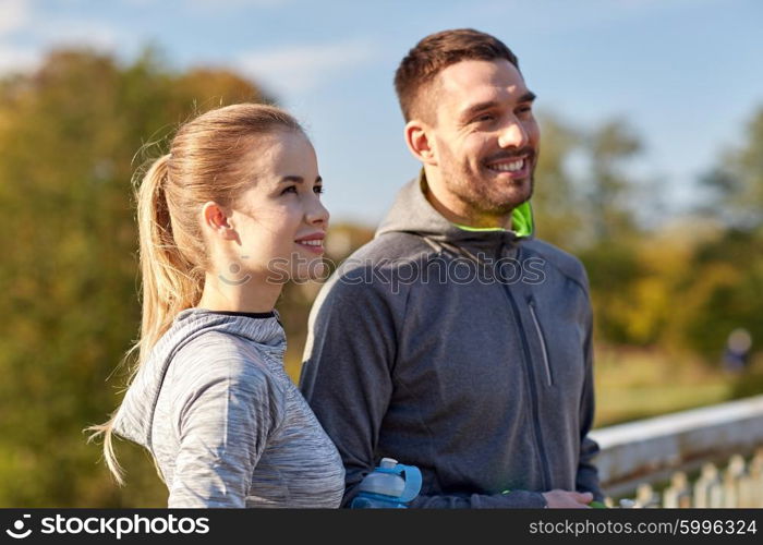 fitness, sport, people and lifestyle concept - smiling couple with bottles of water outdoors