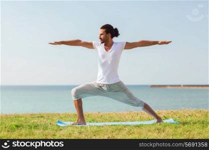 fitness, sport, people and lifestyle concept - smiling man making yoga exercises on mat outdoors