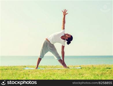 fitness, sport, people and lifestyle concept - smiling man making yoga exercises on mat outdoors