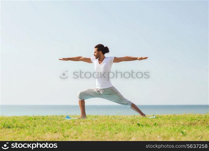 fitness, sport, people and lifestyle concept - smiling man making yoga exercises outdoors