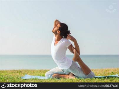fitness, sport, people and lifestyle concept - smiling man making yoga exercises sitting on mat outdoors