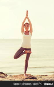 fitness, sport, people and lifestyle concept - smiling woman making yoga exercises on beach