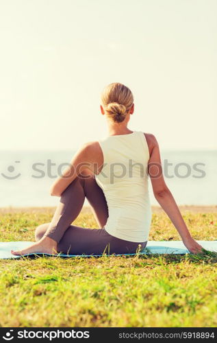 fitness, sport, people and lifestyle concept - woman making yoga exercises on mat outdoors from back