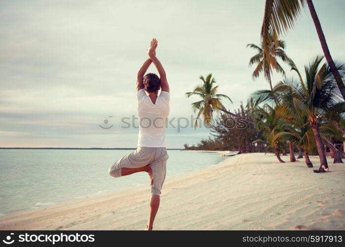 fitness, sport, people and lifestyle concept - young man making yoga exercises on beach from back