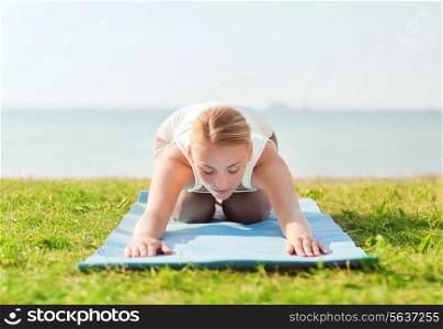 fitness, sport, people and lifestyle concept - young woman making yoga exercises lying on mat outdoors