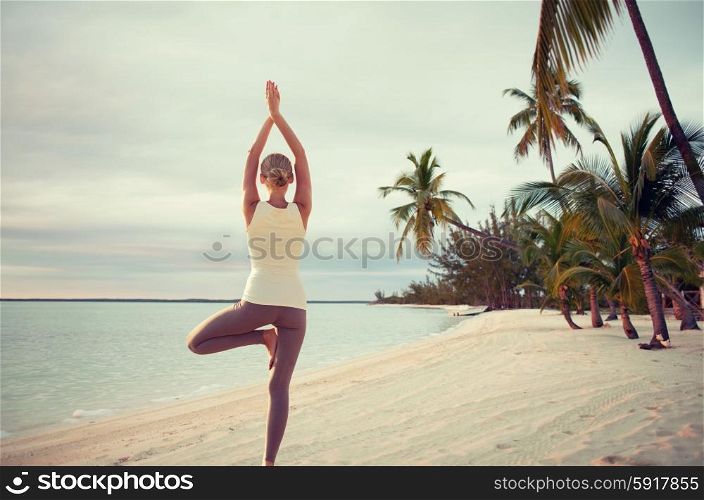 fitness, sport, people and lifestyle concept - young woman making yoga exercises on beach from back