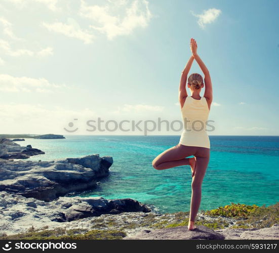 fitness, sport, people and lifestyle concept - young woman making yoga exercises on beach from back