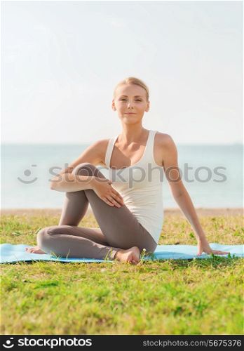 fitness, sport, people and lifestyle concept - young woman making yoga exercises sitting on mat outdoors