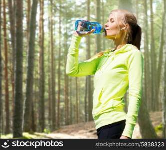 fitness, sport, people and thirst concept - happy woman drinking bottle water after doing sports over woods background