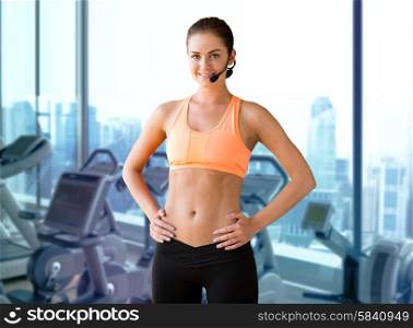 fitness, sport, people and training concept - female sports trainer with microphone over gym machines background