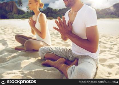 fitness, sport, people and yoga concept - close up of couple meditating in lotus pose outdoors over exotic tropical beach background. close up of couple making yoga exercises outdoors