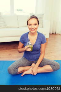 fitness, sport, people, diet and healthy lifestyle concept - happy woman with cup of smoothie sitting on mat at home. happy woman with smoothie sitting on mat at home