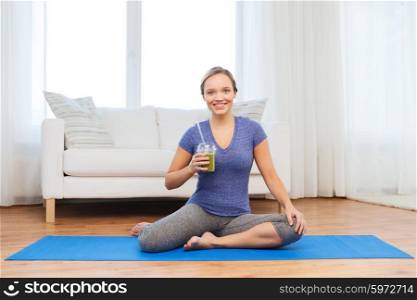 fitness, sport, people, diet and healthy lifestyle concept - happy woman with cup of smoothie sitting on mat at home