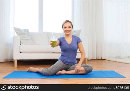 fitness, sport, people, diet and healthy lifestyle concept - happy woman with cup of smoothie sitting on mat at home