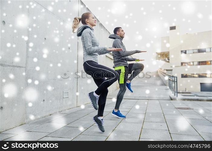 fitness, sport, people, exercising and healthy lifestyle concept - happy man and woman jumping outdoors over snow