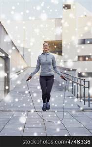 fitness, sport, people, exercising and healthy lifestyle concept - happy woman skipping with jump rope outdoors over snow