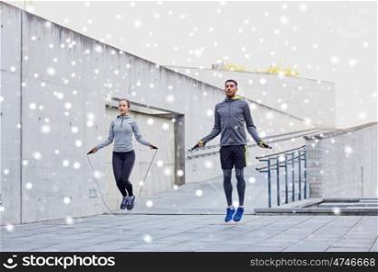 fitness, sport, people, exercising and healthy lifestyle concept - man and woman skipping with jump rope outdoors over snow