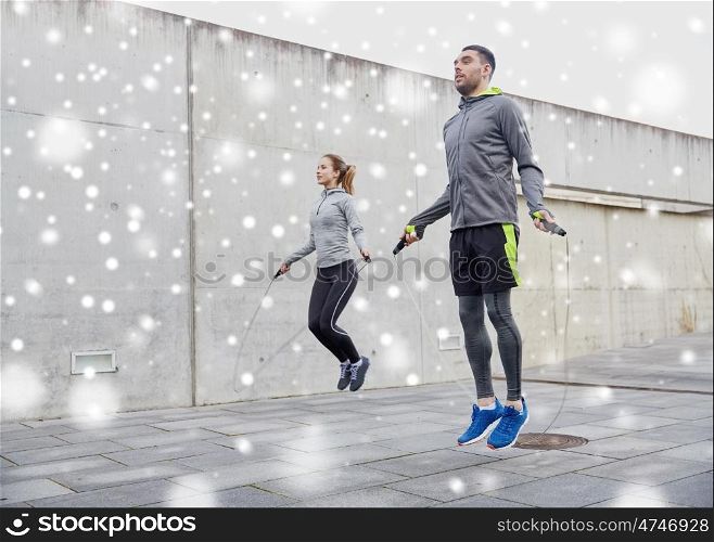 fitness, sport, people, exercising and healthy lifestyle concept - man and woman skipping with jump rope outdoors over snow