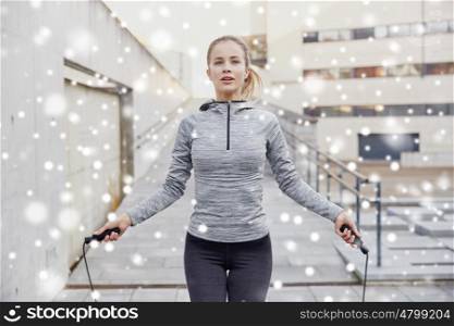 fitness, sport, people, exercising and healthy lifestyle concept - woman skipping with jump rope outdoors over snow