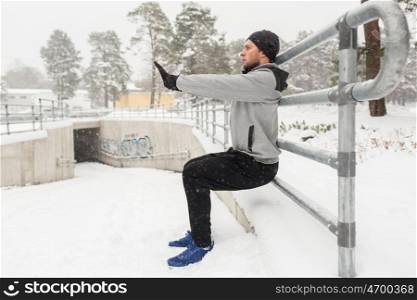 fitness, sport, people, exercising and healthy lifestyle concept - young man doing squats and warmig up at fence in winter